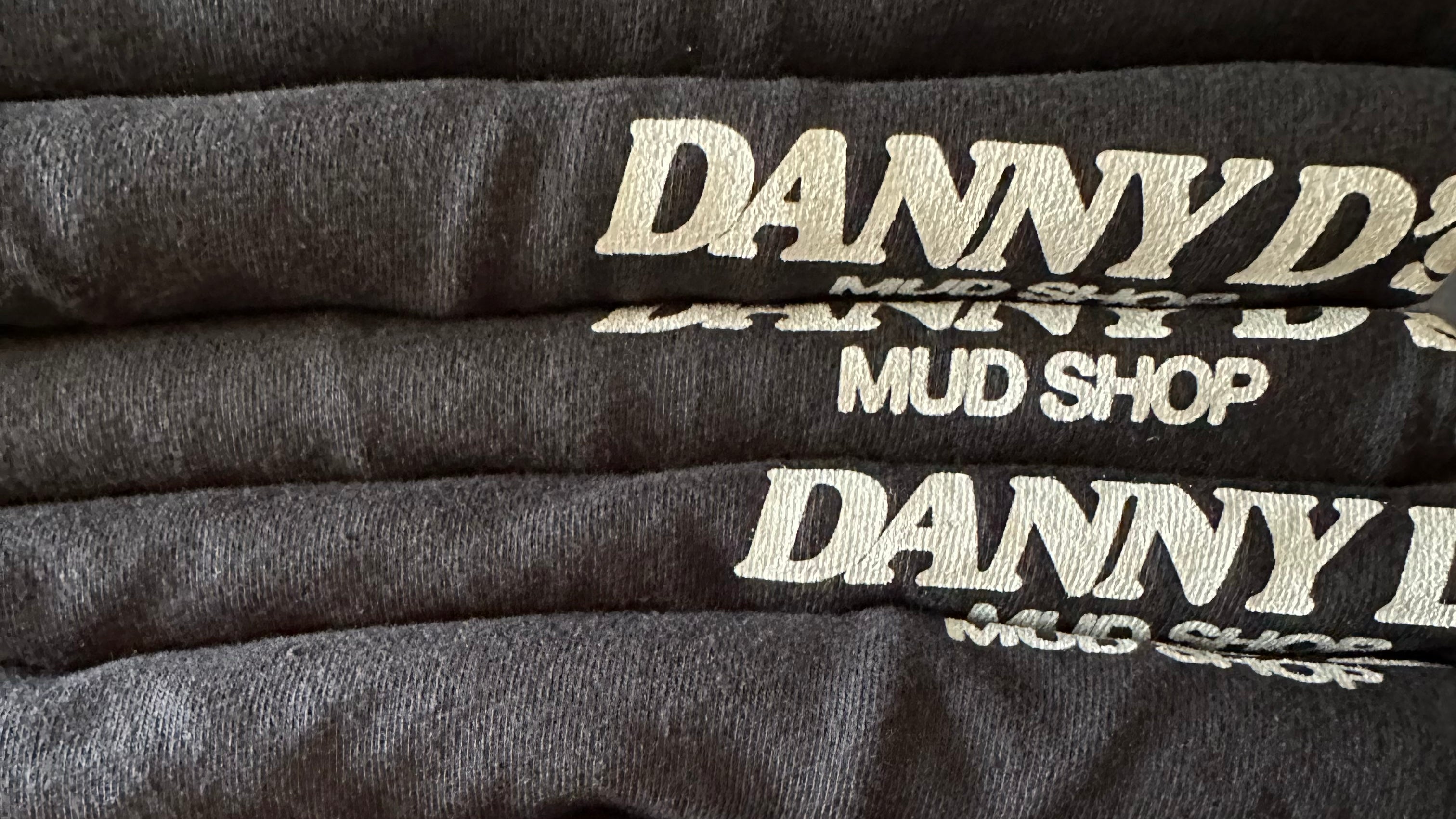 Stack of Danny D's Mud Shop shirts