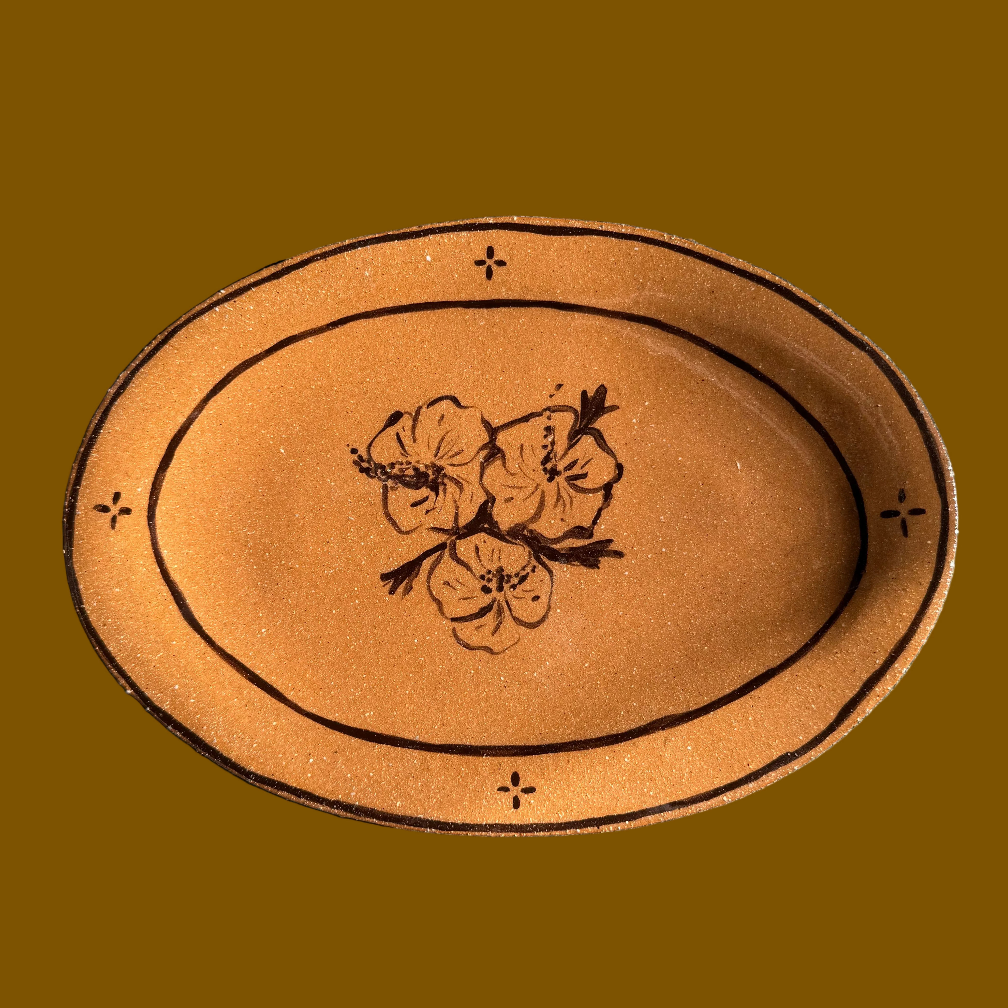 Oval-shaped terracotta plate with floral design on a concrete surface