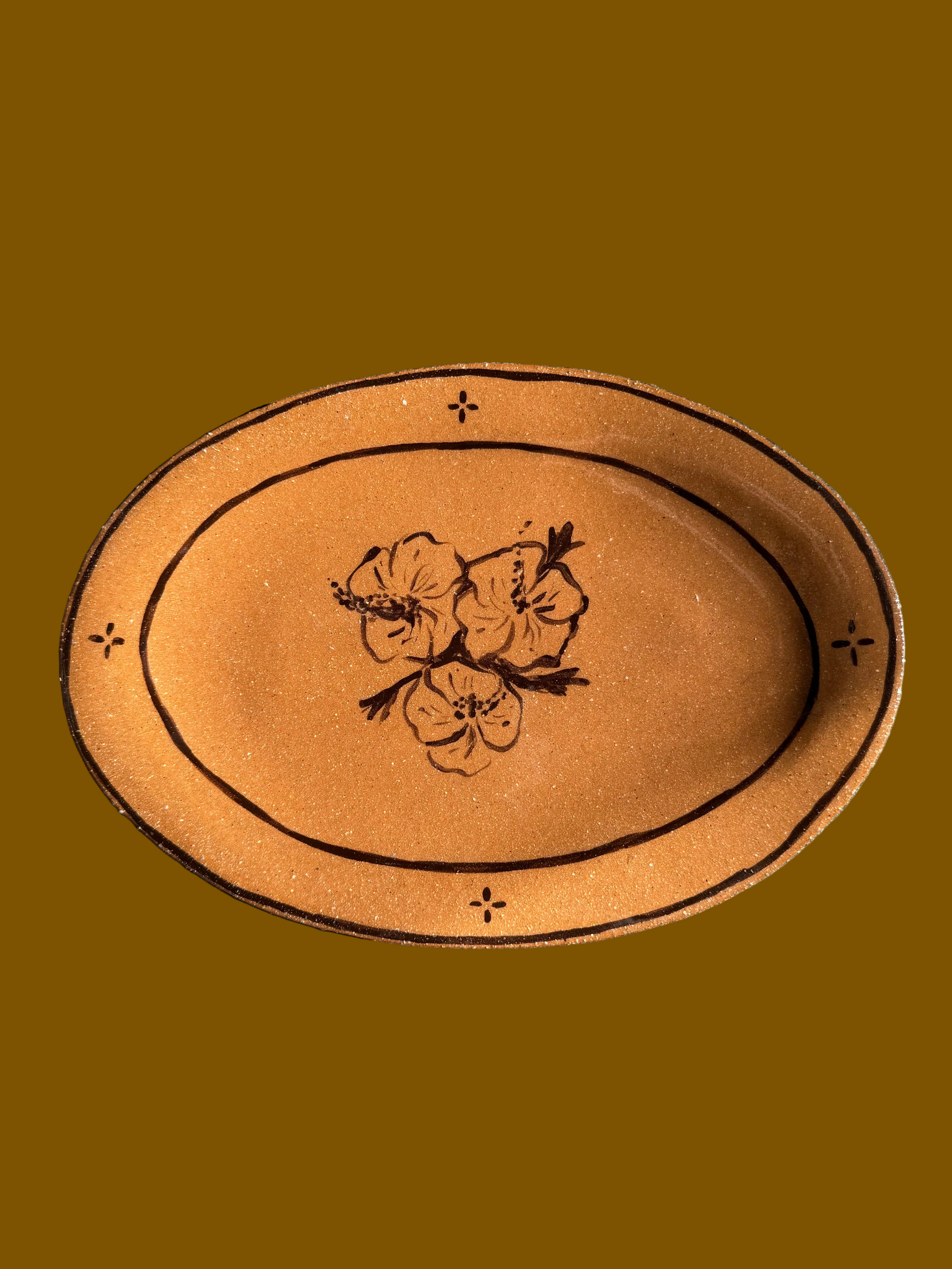 Oval-shaped terracotta plate with floral design on a concrete surface